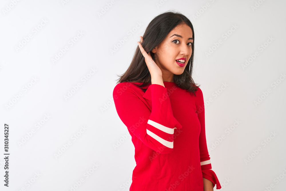 Young beautiful chinese woman wearing red dress standing over isolated white background smiling with hand over ear listening an hearing to rumor or gossip. Deafness concept. Young beautiful chinese woman wearing red dress standing over isolated white background smiling with hand over ear listening an hearing to rumor or gossip. Deafness concept.