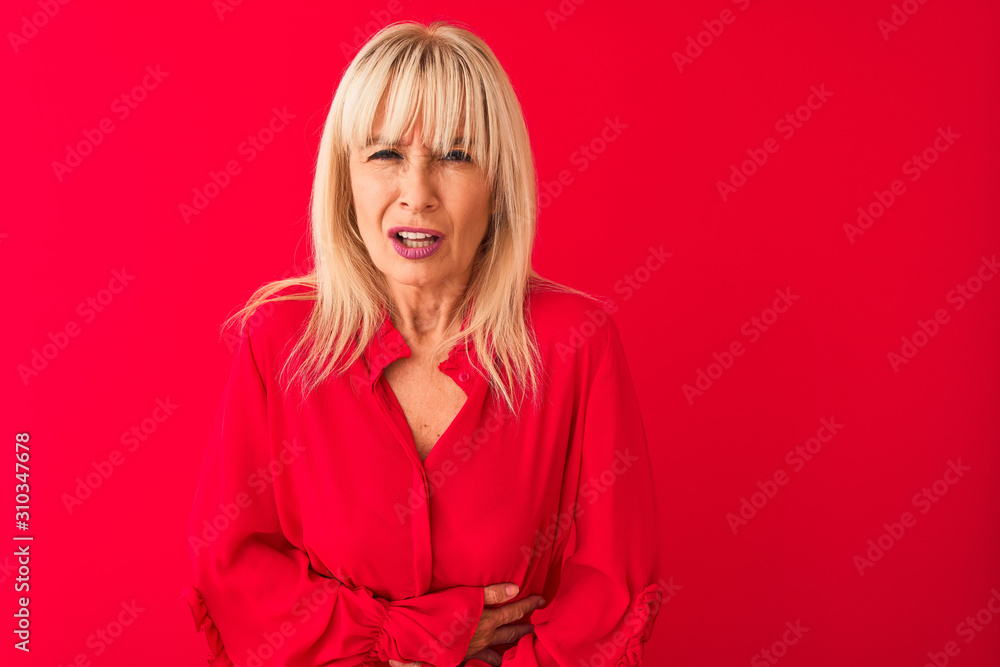 Fototapeta premium Middle age woman wearing elegant shirt standing over isolated red background with hand on stomach because nausea, painful disease feeling unwell. Ache concept.