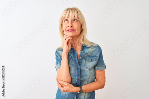 Middle age woman wearing casual denim shirt standing over isolated white background with hand on chin thinking about question, pensive expression. Smiling with thoughtful face. Doubt concept.