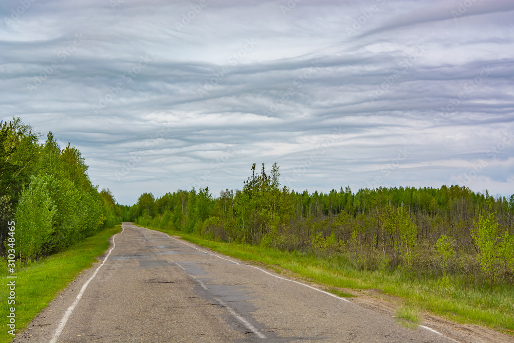 Wavy clouds in the sky. Old asphalt road.
