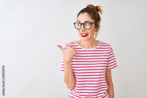 Redhead woman wearing glasses striped t-shirt and pigtail over isolated white background smiling with happy face looking and pointing to the side with thumb up.