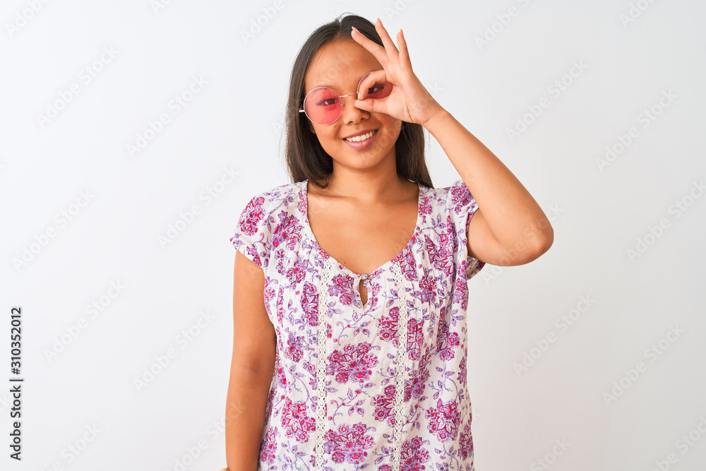 Young chinese woman wearing floral t-shirt and pink glasses over isolated white background doing ok gesture with hand smiling, eye looking through fingers with happy face. Young chinese woman wearing floral t-shirt and pink glasses over isolated white background doing ok gesture with hand smiling, eye looking through fingers with happy face.