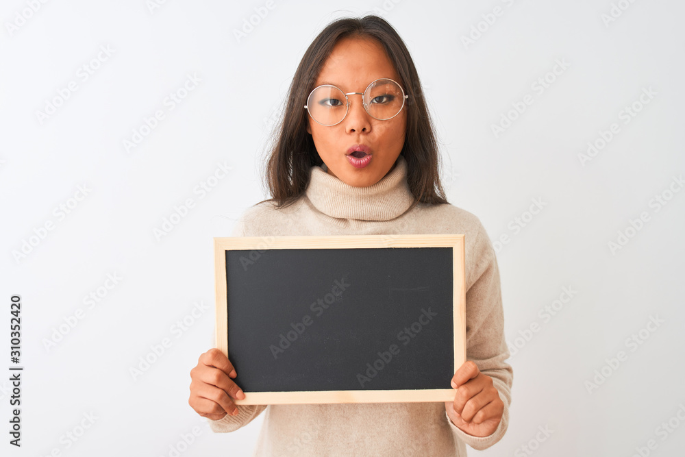 Young chinese woman wearing glasses holding blackboard over isolated white background scared in shock with a surprise face, afraid and excited with fear expression Young chinese woman wearing glasses holding blackboard over isolated white background scared in shock with a surprise face, afraid and excited with fear expression