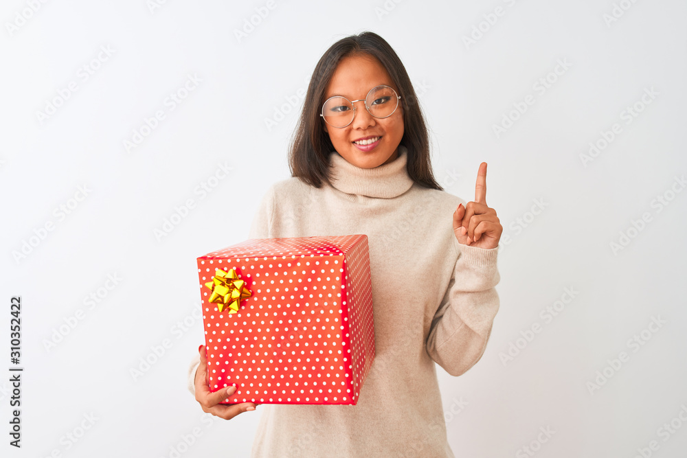 Young chinese woman wearing glasses holding birthday gift over isolated white background surprised with an idea or question pointing finger with happy face, number one Young chinese woman wearing glasses holding birthday gift over isolated white background surprised with an idea or question pointing finger with happy face, number one