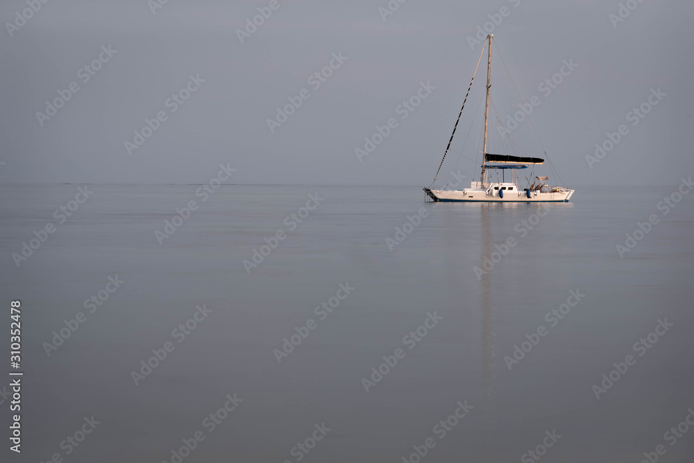 Anchored Caribbean sailboat at dusk on isolated simple background.