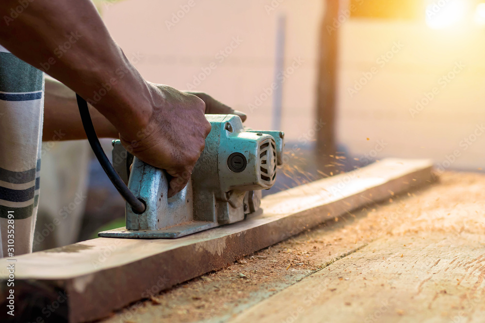 Close-up of a carpenter's hand using a planer on a wooden floor and creating dust from work.