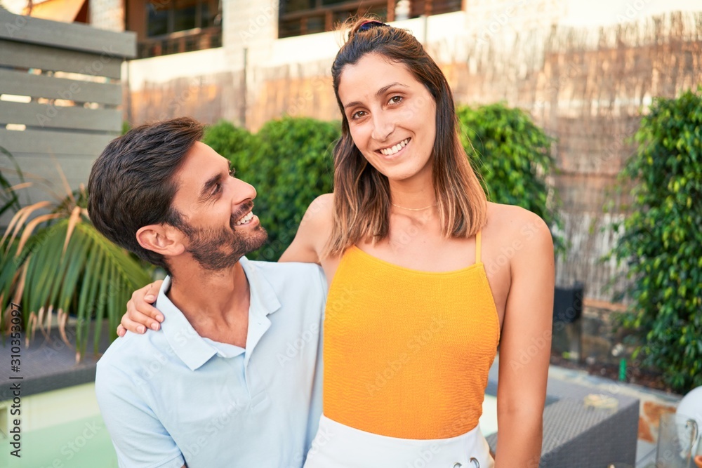 Young beautiful couple on vacation smiling happy and confident. Standing with smile on face hugging at the beach club Young beautiful couple on vacation smiling happy and confident. Standing with smile on face hugging at the beach club