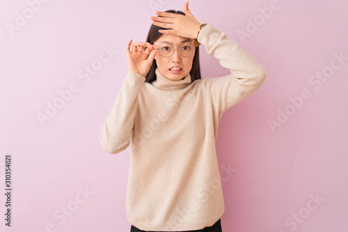 Young chinese woman wearing turtleneck sweater and glasses over isolated pink background stressed with hand on head, shocked with shame and surprise face, angry and frustrated. Fear and upset