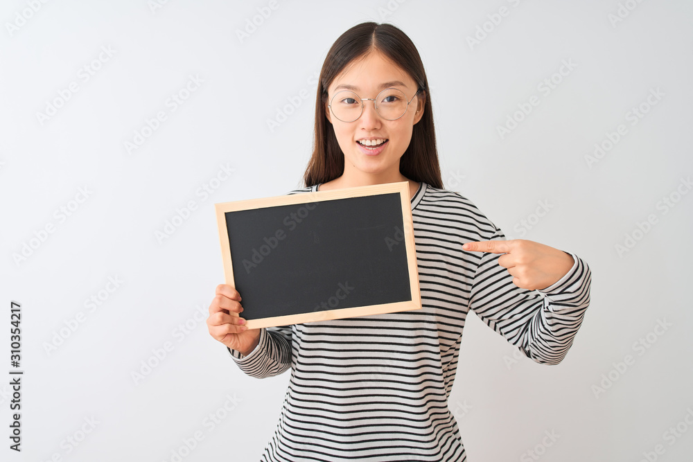 Young chinese woman wearing glasses holding blackboard over isolated white background very happy pointing with hand and finger Young chinese woman wearing glasses holding blackboard over isolated white background very happy pointing with hand and finger