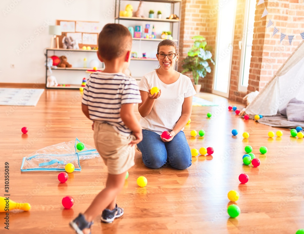 Fototapeta premium Beautiful teacher and toddler boy playing with colored small balls at kindergarten