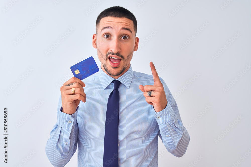 Young business man holding credit card over isolated background surprised with an idea or question pointing finger with happy face, number one Young business man holding credit card over isolated background surprised with an idea or question pointing finger with happy face, number one