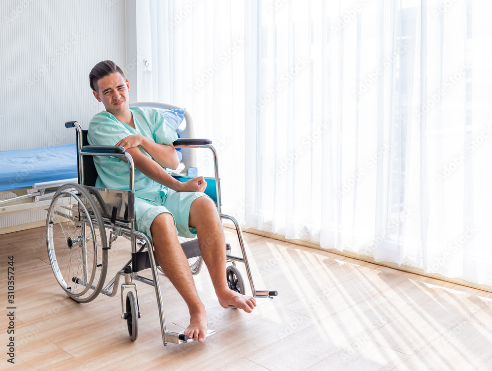 Asian Young man patient sitting in a wheelchair in injury posture on hospital room background. Health and Personal Accident Insurance concept. Asian Young man patient sitting in a wheelchair in injury posture on hospital room background. Health and Personal Accident Insurance concept.