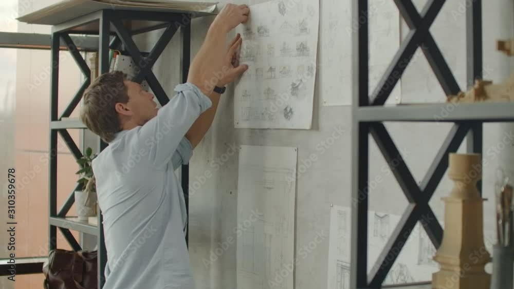 Designer works in loft office and makes notes on the drawings on wall. Designer works in loft office and makes notes on the drawings on the wall