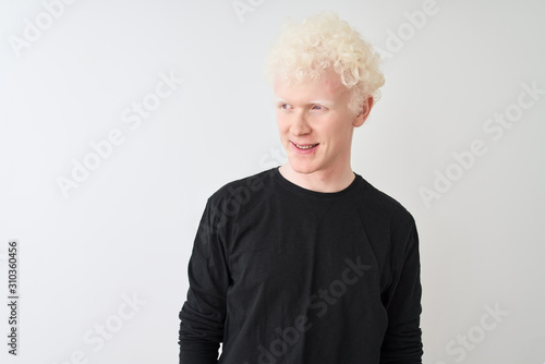 Young albino blond man wearing black t-shirt standing over isolated white background looking away to side with smile on face, natural expression. Laughing confident.