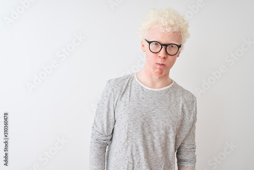 Young albino blond man wearing striped t-shirt and glasses over isolated white background puffing cheeks with funny face. Mouth inflated with air, crazy expression.