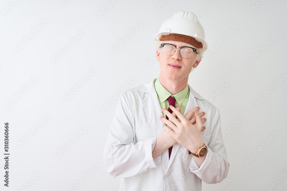 Albino scientist man wearing glasses and helmet standing over isolated white background smiling with hands on chest with closed eyes and grateful gesture on face. Health concept. Albino scientist man wearing glasses and helmet standing over isolated white background smiling with hands on chest with closed eyes and grateful gesture on face. Health concept.