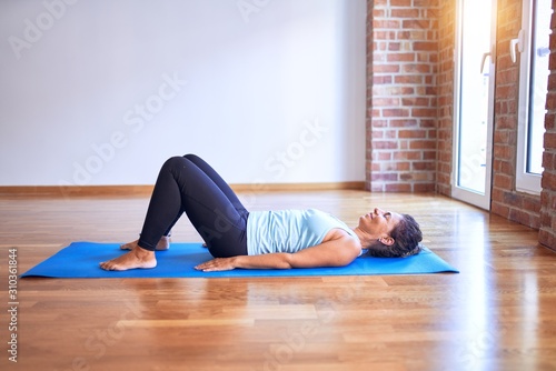 Middle age beautiful sportwoman smiling happy. Lying down on mat practicing yoga doing bridge pose at gym photo