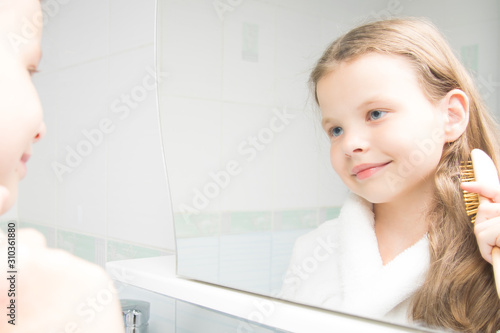 a girl in a white robe, in the bathroom, combing her hair, looking in the mirror and smiling