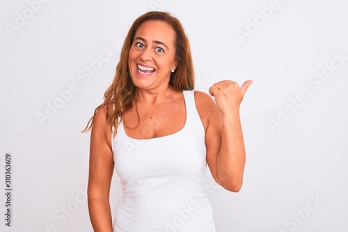 Middle age mature woman standing over white isolated background smiling with happy face looking and pointing to the side with thumb up. © Krakenimages.com