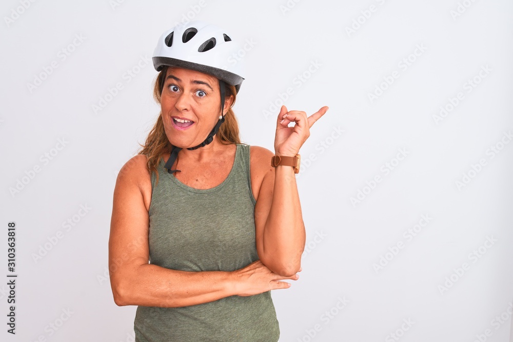 Middle age mature cyclist woman wearing safety helmet over isolated background with a big smile on face, pointing with hand finger to the side looking at the camera. Middle age mature cyclist woman wearing safety helmet over isolated background with a big smile on face, pointing with hand finger to the side looking at the camera.