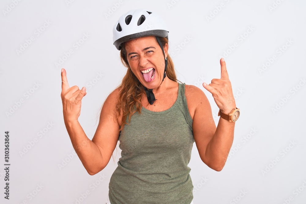 Middle age mature cyclist woman wearing safety helmet over isolated background shouting with crazy expression doing rock symbol with hands up. Music star. Heavy music concept. Middle age mature cyclist woman wearing safety helmet over isolated background shouting with crazy expression doing rock symbol with hands up. Music star. Heavy music concept.