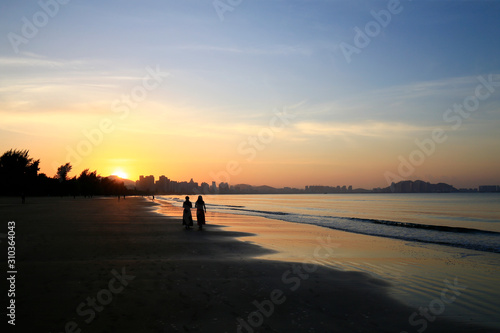Two women by the sea, silhouetted by the sunrise