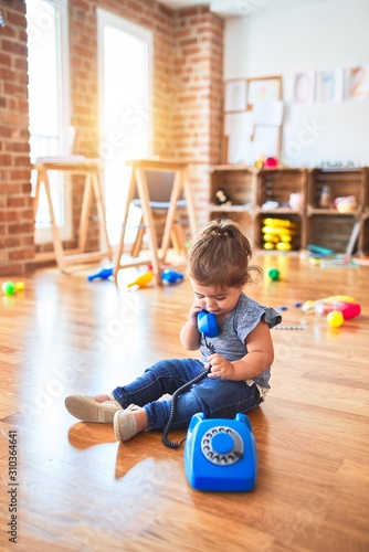 Beautiful toddler sitting on the floor playing with vintage phone at kindergarten