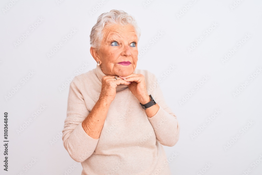 Senior grey-haired woman wearing turtleneck sweater standing over isolated white background laughing nervous and excited with hands on chin looking to the side Senior grey-haired woman wearing turtleneck sweater standing over isolated white background laughing nervous and excited with hands on chin looking to the side