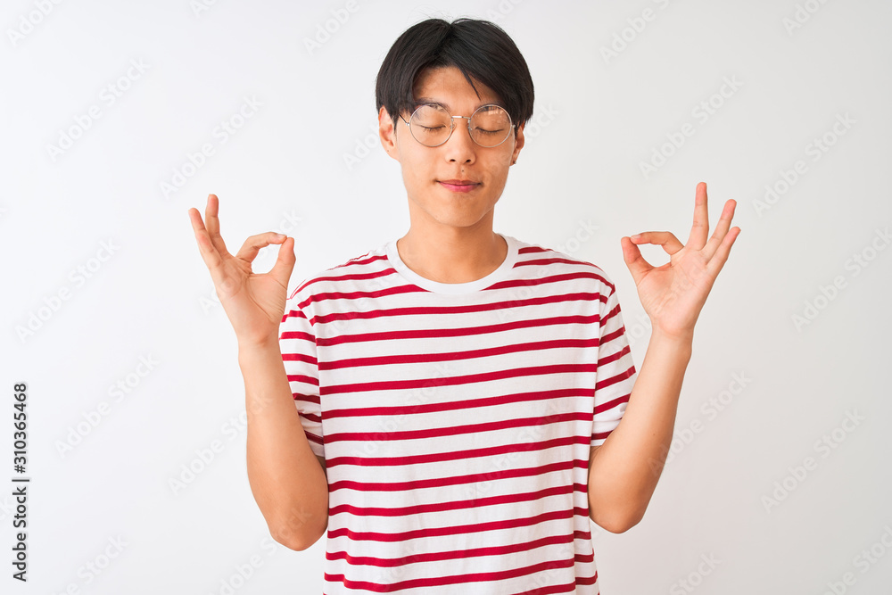 Young chinese man wearing glasses and striped t-shirt standing over isolated white background relax and smiling with eyes closed doing meditation gesture with fingers. Yoga concept. Young chinese man wearing glasses and striped t-shirt standing over isolated white background relax and smiling with eyes closed doing meditation gesture with fingers. Yoga concept.