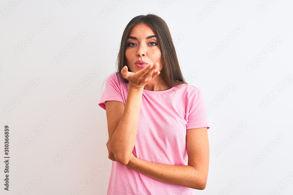 Young beautiful woman wearing pink casual t-shirt standing over isolated white background looking at the camera blowing a kiss with hand on air being lovely and sexy. Love expression. Young beautiful woman wearing pink casual t-shirt standing over isolated white background looking at the camera blowing a kiss with hand on air being lovely and sexy. Love expression.