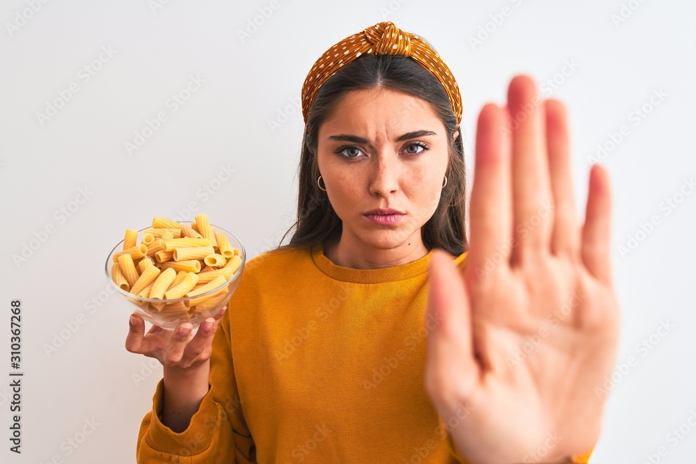Young beautiful woman holding bowl with macaroni pasta over isolated white background with open hand doing stop sign with serious and confident expression, defense gesture Young beautiful woman holding bowl with macaroni pasta over isolated white background with open hand doing stop sign with serious and confident expression, defense gesture
