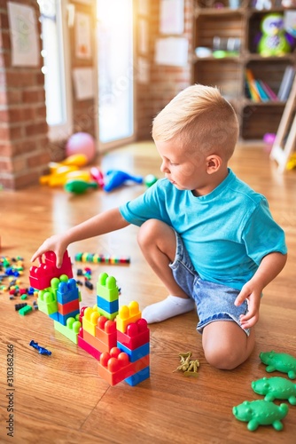 Young caucasian kid playing at kindergarten with toys. Preschooler boy happy at playroom.