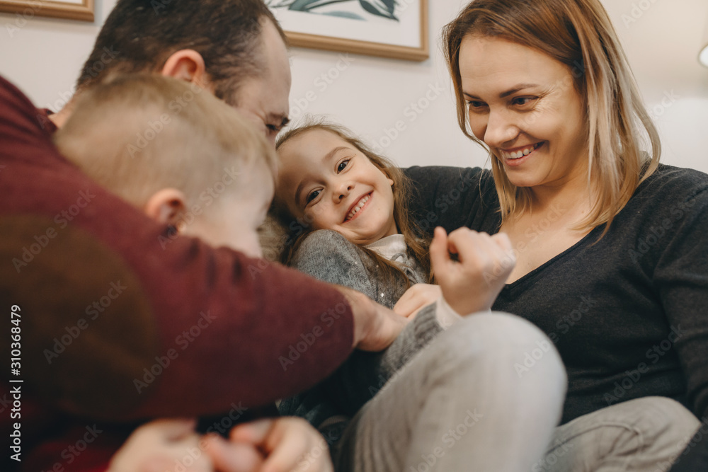 Beautiful big family embracing and having fun on the couch at their home while little girl is looking at camera smiling.