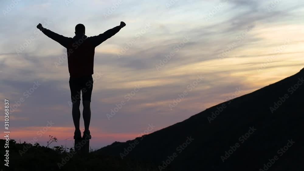 Dark silhouette of a hiker climbing a mountain at sunset and raising his hands reaching summit like a winner. Dark silhouette of a hiker climbing a mountain at sunset and raising his hands reaching summit like a winner.