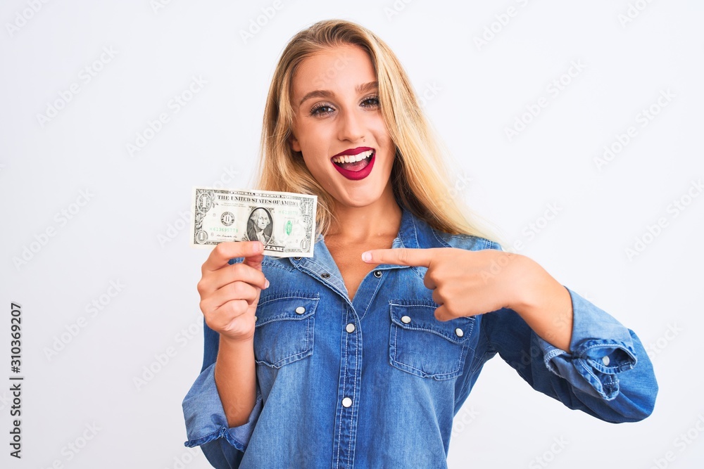 Young beautiful blond woman holding dollar standing over isolated white background very happy pointing with hand and finger Young beautiful blond woman holding dollar standing over isolated white background very happy pointing with hand and finger