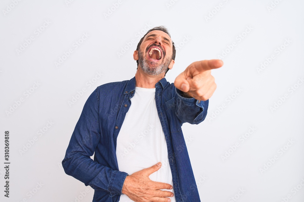 Middle age handsome man wearing blue denim shirt standing over isolated white background laughing at you, pointing finger to the camera with hand over body, shame expression Middle age handsome man wearing blue denim shirt standing over isolated white background laughing at you, pointing finger to the camera with hand over body, shame expression