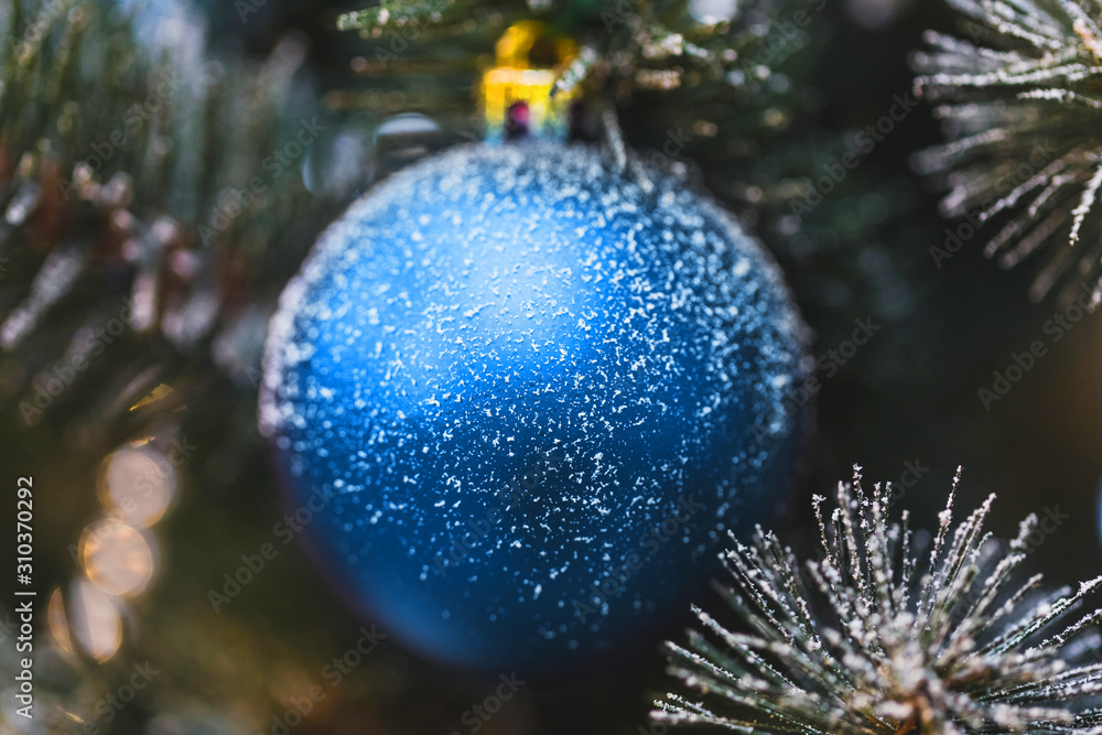 Beautiful New Year decorations, blue shining ball in snow close-up on Christmas tree. Trendy classic color of 2020.