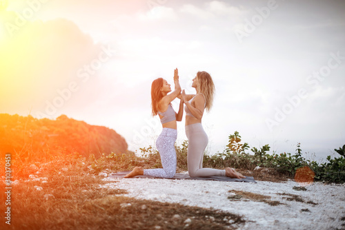 Pair of girls practice yoga against the background of the ocean