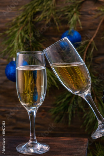 Glasses of champagne with bubbles on the background of Christmas decorations. Glasses touch during a festive toast. Beautiful card.