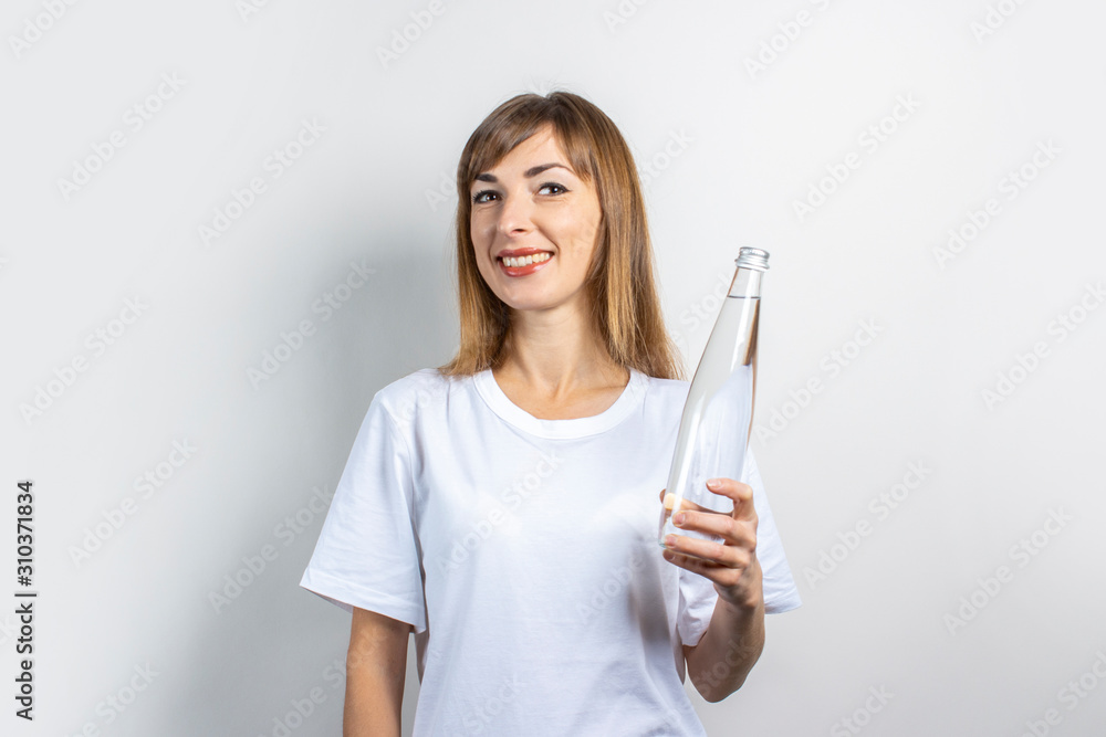Young woman holds a bottle with clear water on a light background. Banner. The concept of thirst, heat, health and beauty care, water balance Young woman holds a bottle with clear water on a light background. Banner. The concept of thirst, heat, health and beauty care, water balance