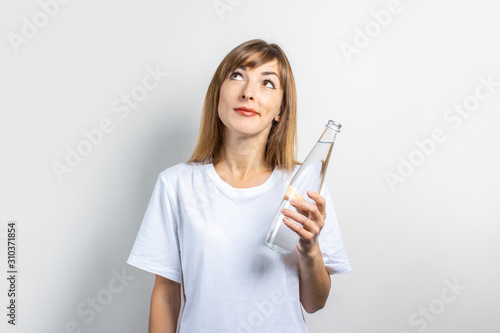Young woman holds a bottle with clear water on a light background. Banner. The concept of thirst, heat, health and beauty care, water balance