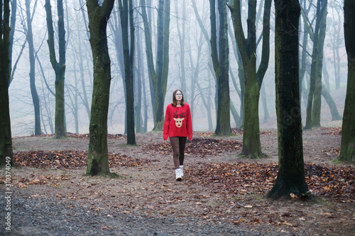 The young girl in the red sweater is walking alone in the cold foggy forest