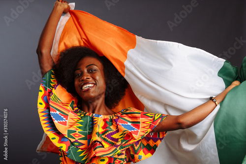 Tablou pe pânză Happy african woman in national clothes smiling and posing with a flag Ivory Coa