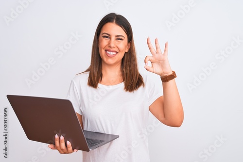 Schilderij op canvas Beautiful young woman working using computer laptop over white background smiling positive doing ok sign with hand and fingers