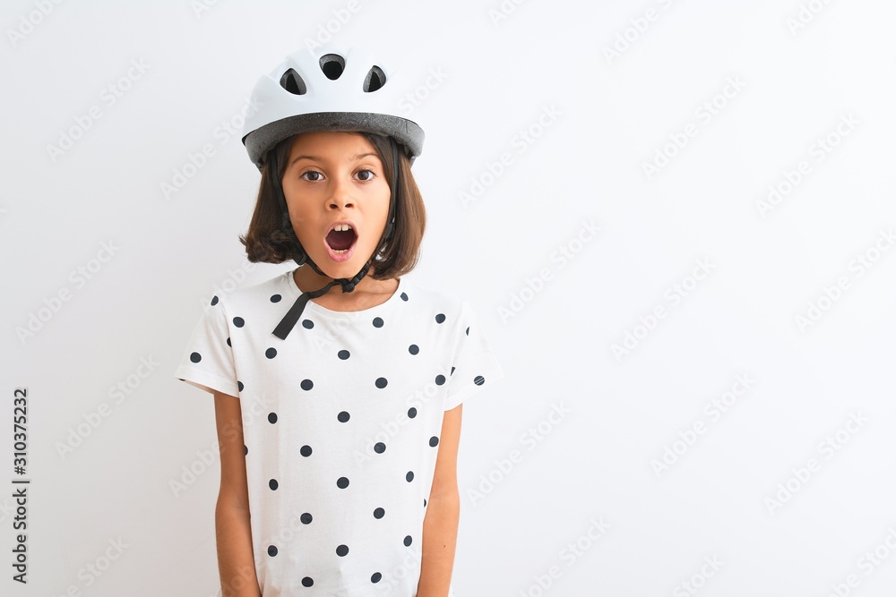 Beautiful child girl wearing security bike helmet standing over isolated white background afraid and shocked with surprise expression, fear and excited face. Beautiful child girl wearing security bike helmet standing over isolated white background afraid and shocked with surprise expression, fear and excited face.