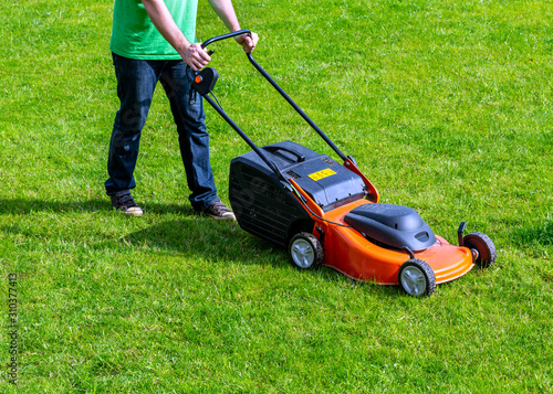 Man in motion with lawnmower and mows green grass