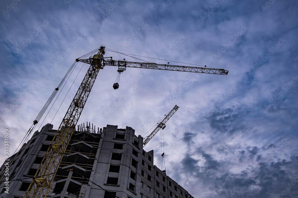 Tower cranes and unfinished multi-storey high buildings under construction site in the evening with dramatic colorful cloud background Tower cranes and unfinished multi-storey high buildings under construction site in the evening with dramatic colorful cloud background