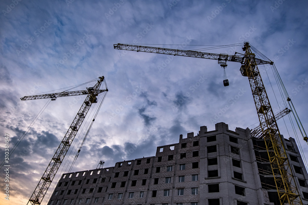 Tower cranes and unfinished multi-storey high buildings under construction site in the evening with dramatic colorful cloud background Tower cranes and unfinished multi-storey high buildings under construction site in the evening with dramatic colorful cloud background