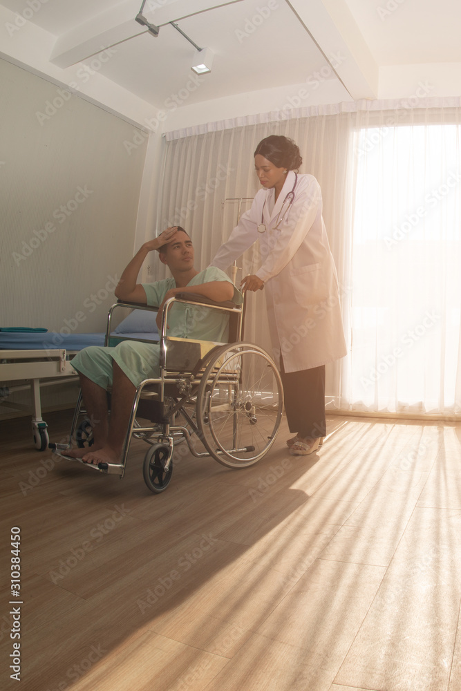 The African female doctor was pushing a wheelchair with a Caucasian male patient sitting for examination. With attention.