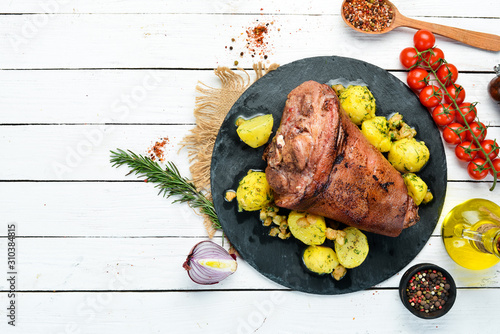 Photography Baked pork leg with potatoes on a black stone plate